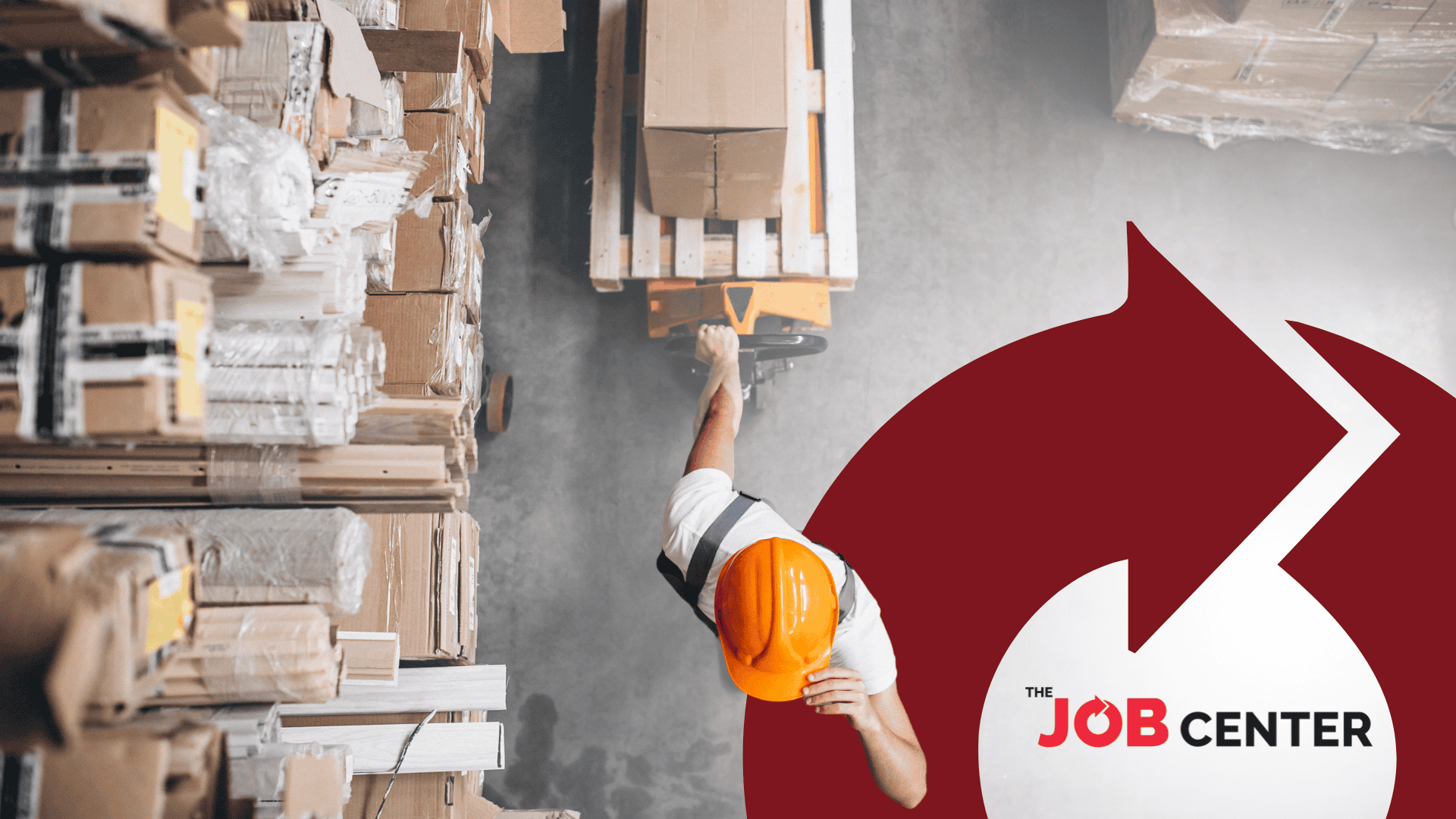 Viewed from above, a warehouse worker in an orange safety helmet pulls a laden trolley