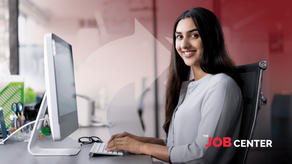 Woman in corporate attire at a long desk speaks to someone, gesturing to printed charts in her hand