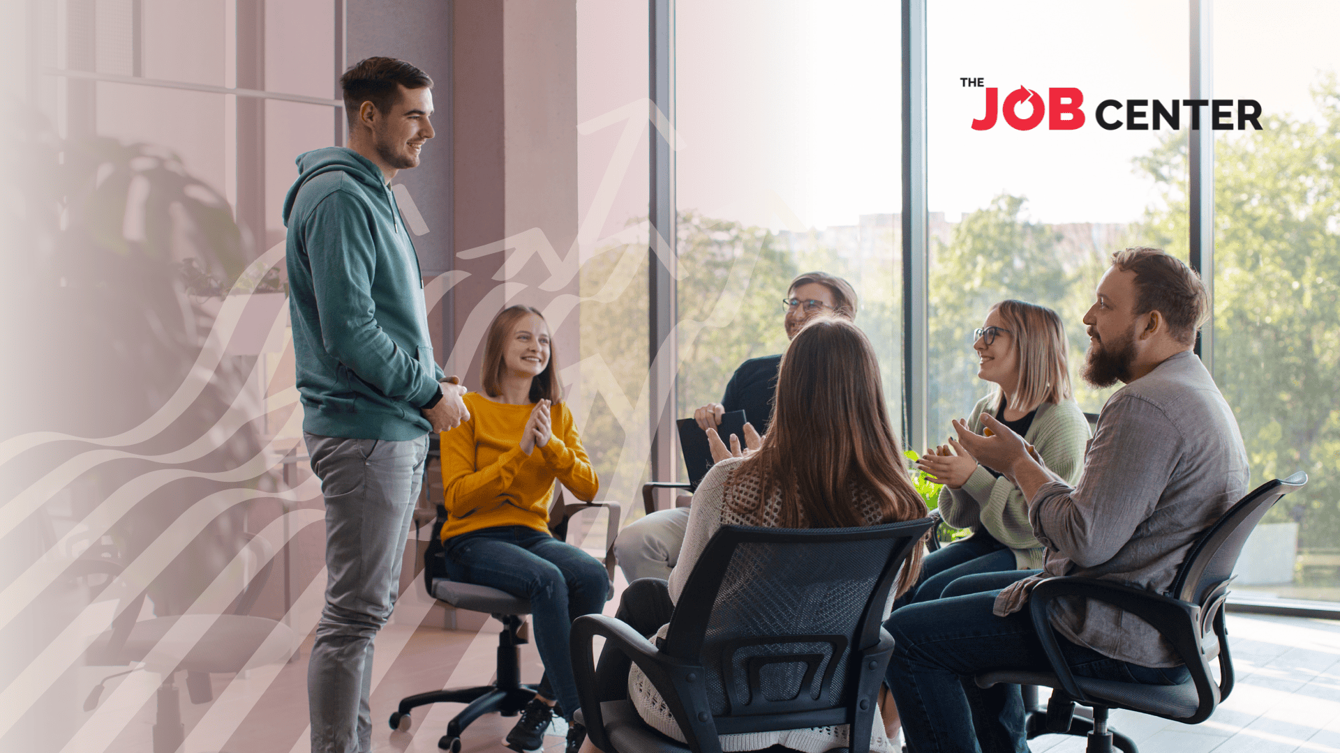 A group of employees sits in a circle of office chairs, applauding one standing employee